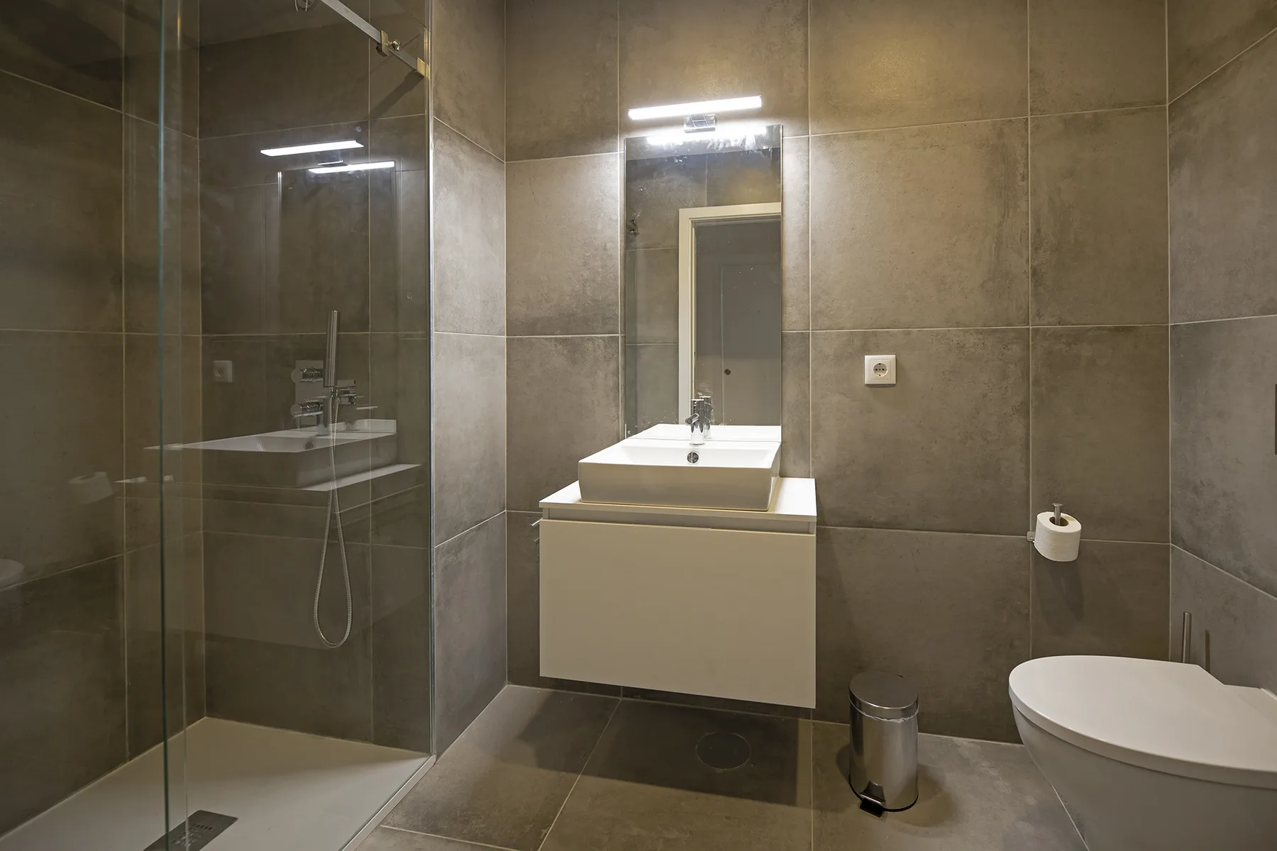 Un baño con azulejos, ducha de vidrio, lavabo e inodoro.