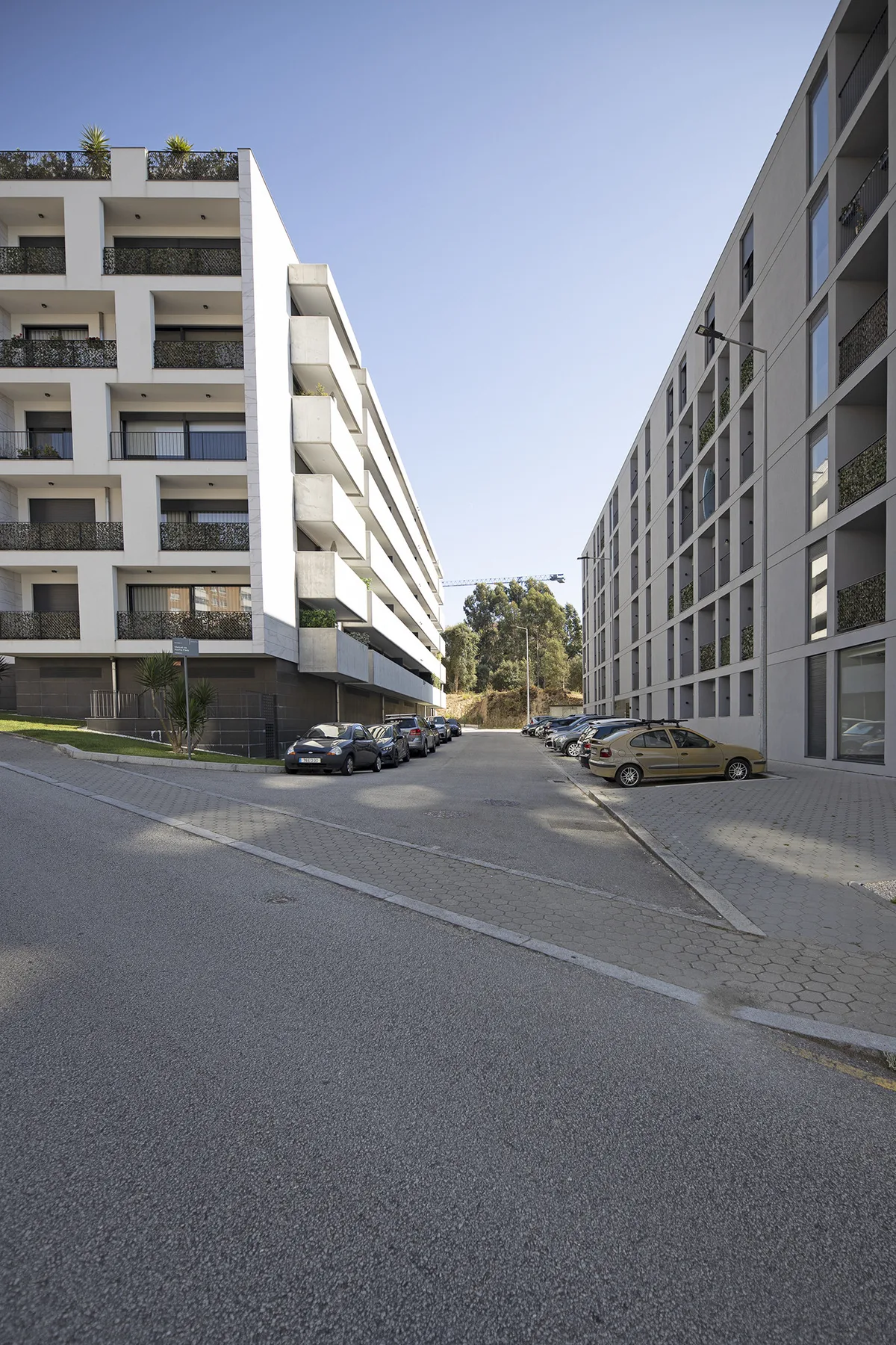 Una calle pasa entre edificios de apartamentos modernos, con coches estacionados junto a la acera.