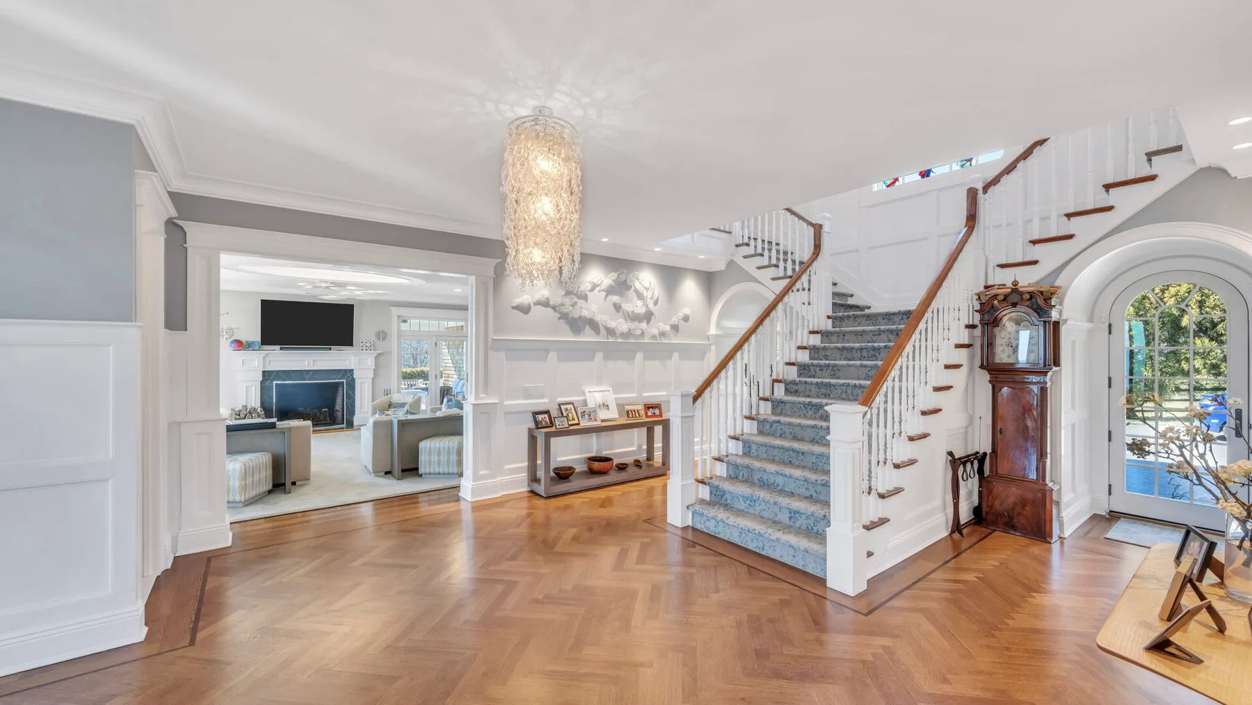 Un recibidor luminoso presenta una escalera curva y un suelo de madera con dibujos.
