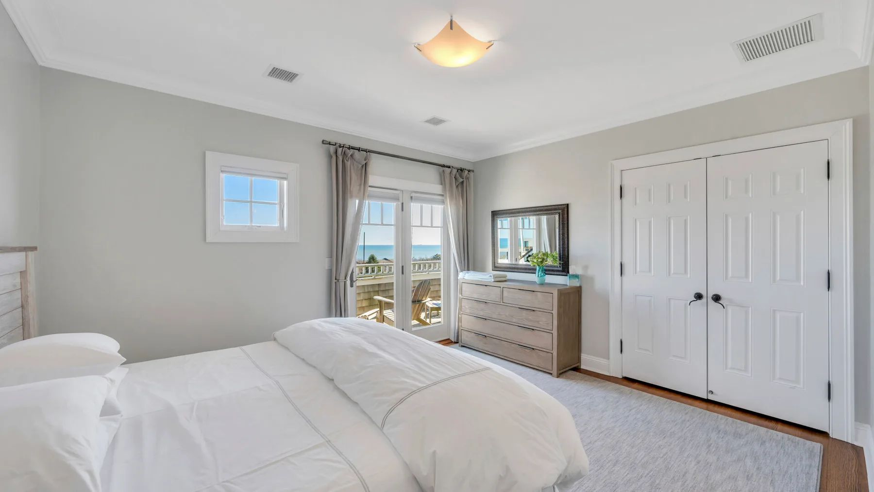 Un dormitorio luminoso con cama, cómoda y puertas dobles.