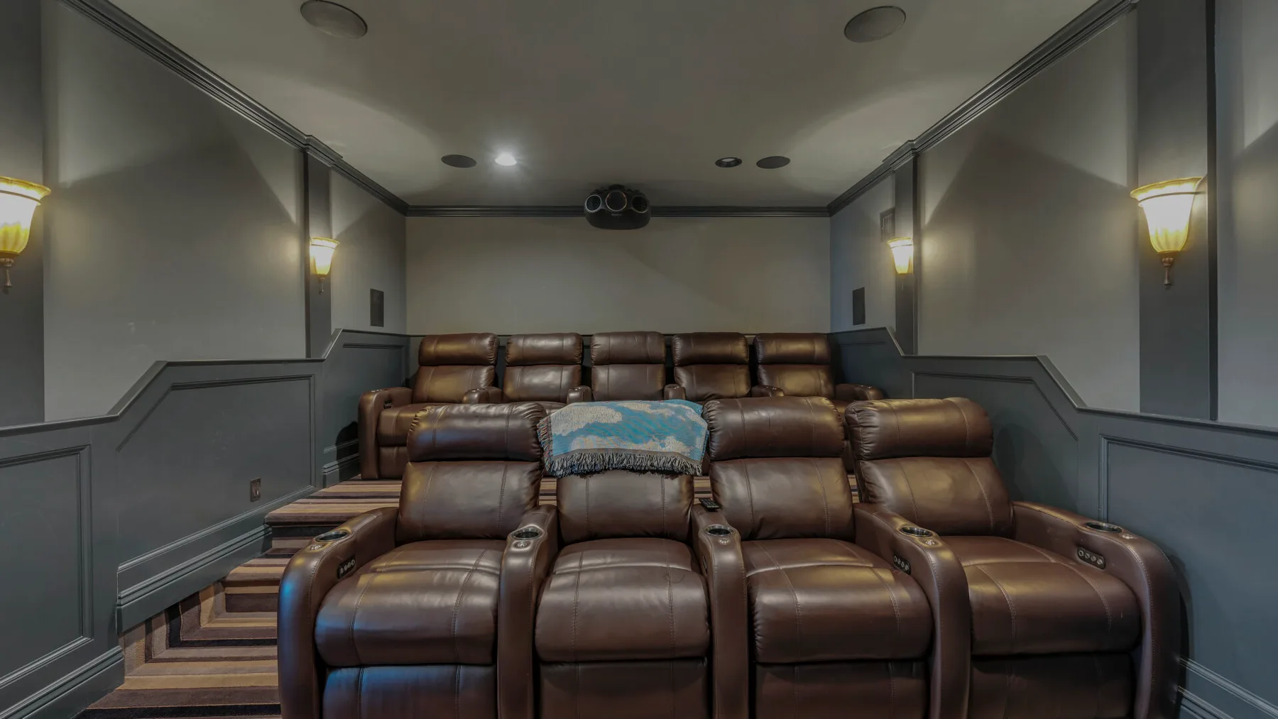 Una sala de cine en casa con filas de asientos reclinables marrones y una pantalla grande.