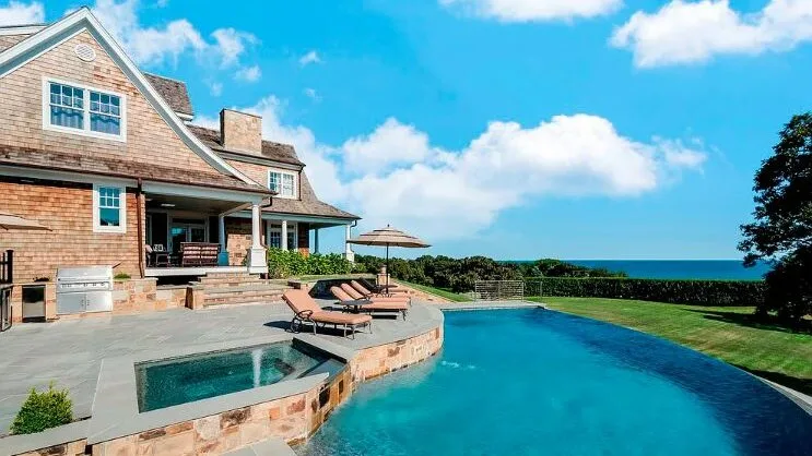 Una casa y una piscina dan al océano bajo un cielo parcialmente nublado.
