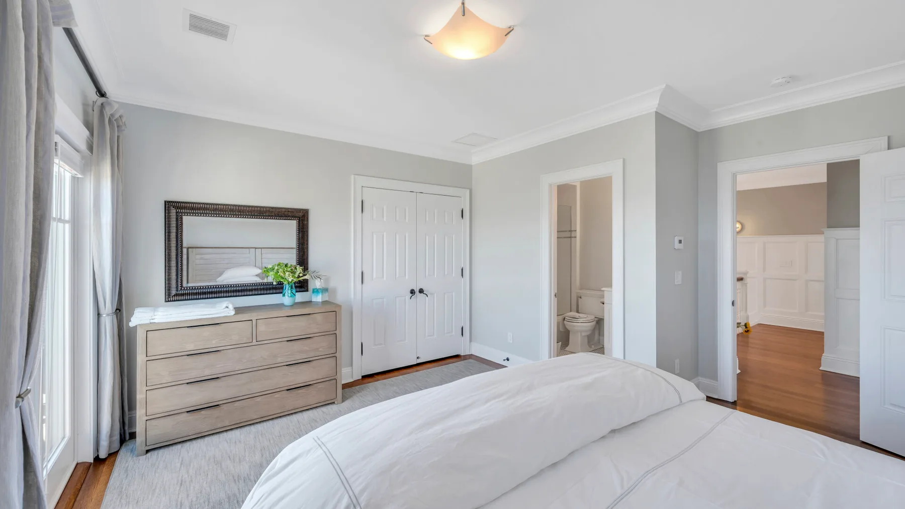 Un dormitorio luminoso con una cama, una cómoda y puertas blancas de armario.