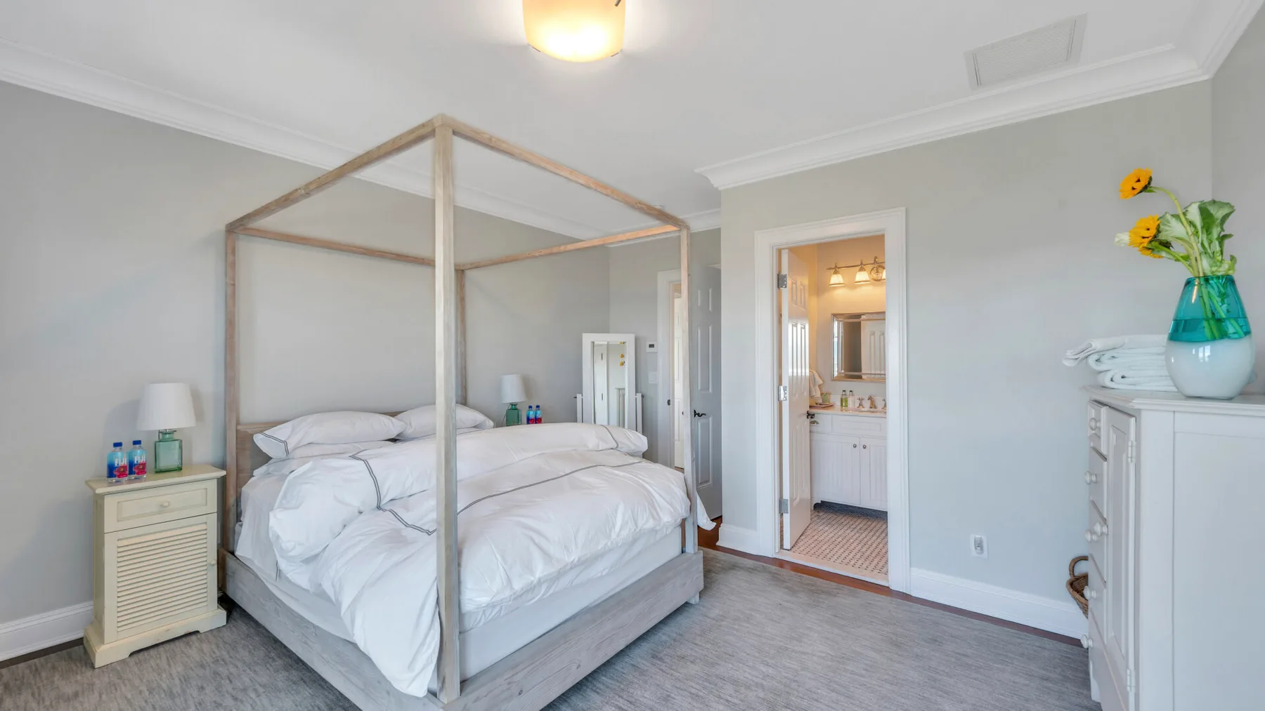 Un dormitorio luminoso con una cama con dosel y una puerta hacia un baño.