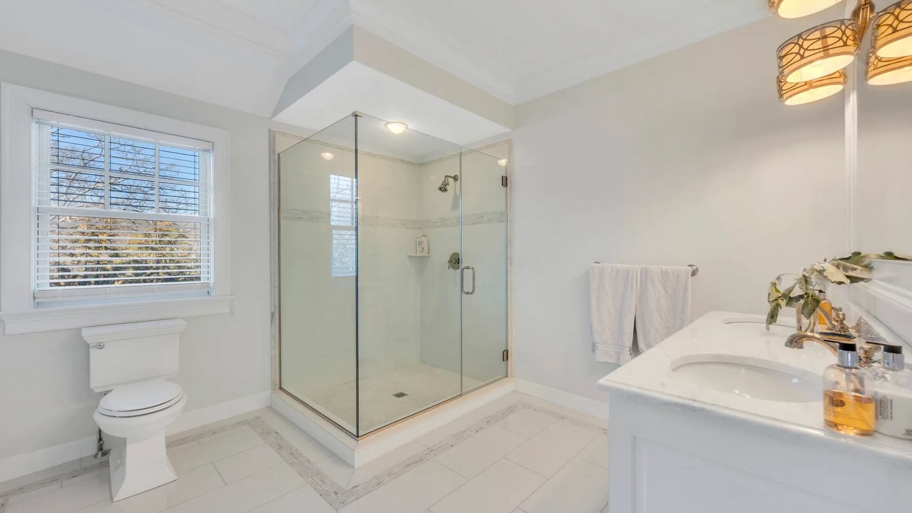 Un baño luminoso con ducha de vidrio, una ventana y un lavabo.