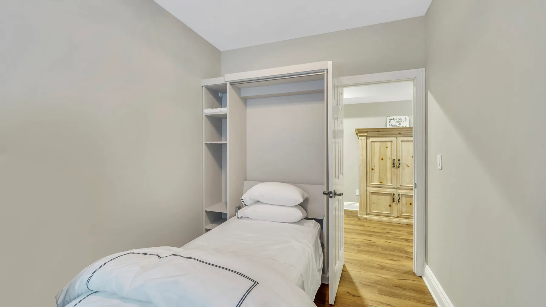 Un dormitorio con una cama individual junto a una puerta abierta que da a una habitación con suelo de madera.