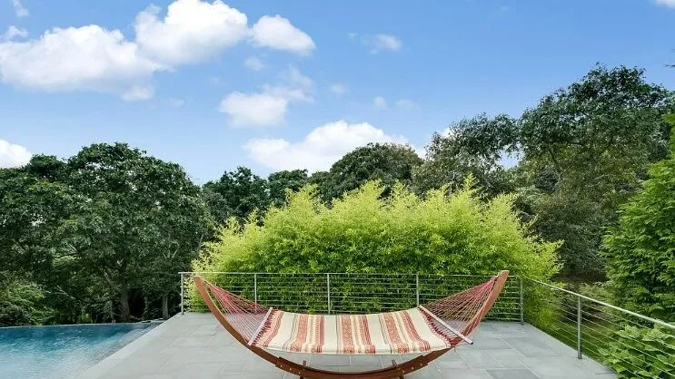 Una terraza exterior da a la vegetación, con una hamaca a rayas junto a la barandilla.