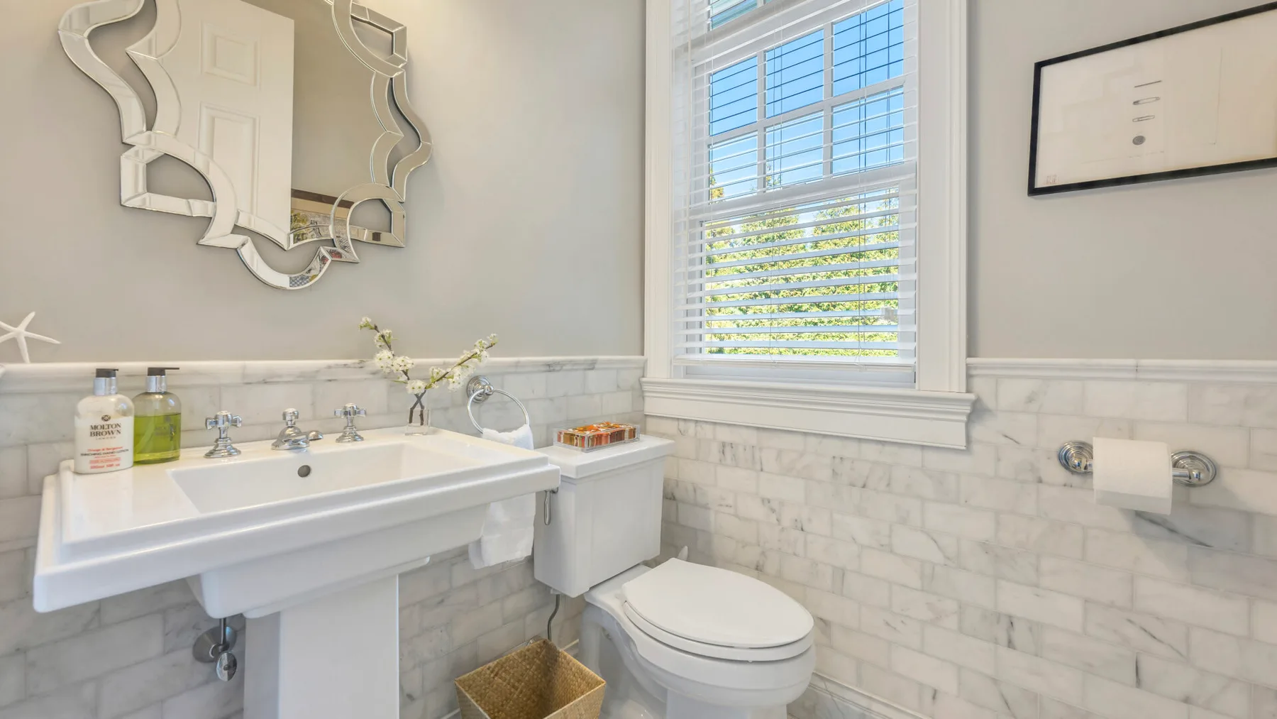 Un baño luminoso con lavabo, inodoro y una ventana con persianas.
