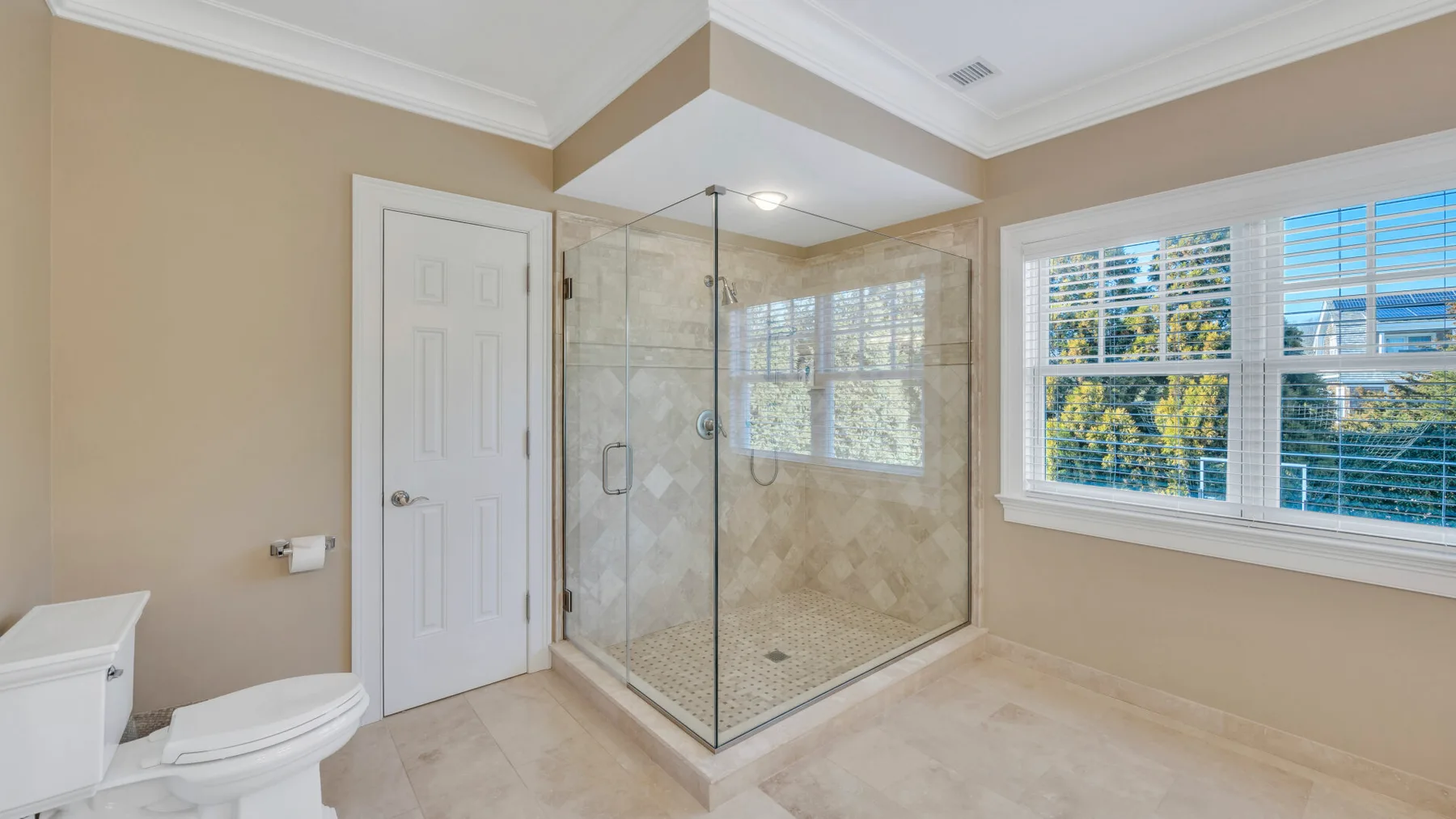 Un baño luminoso con ducha de vidrio y ventanas grandes.