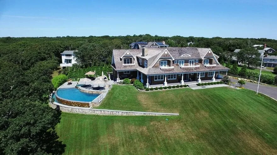 A large house sits beside a curved swimming pool and broad green lawn.