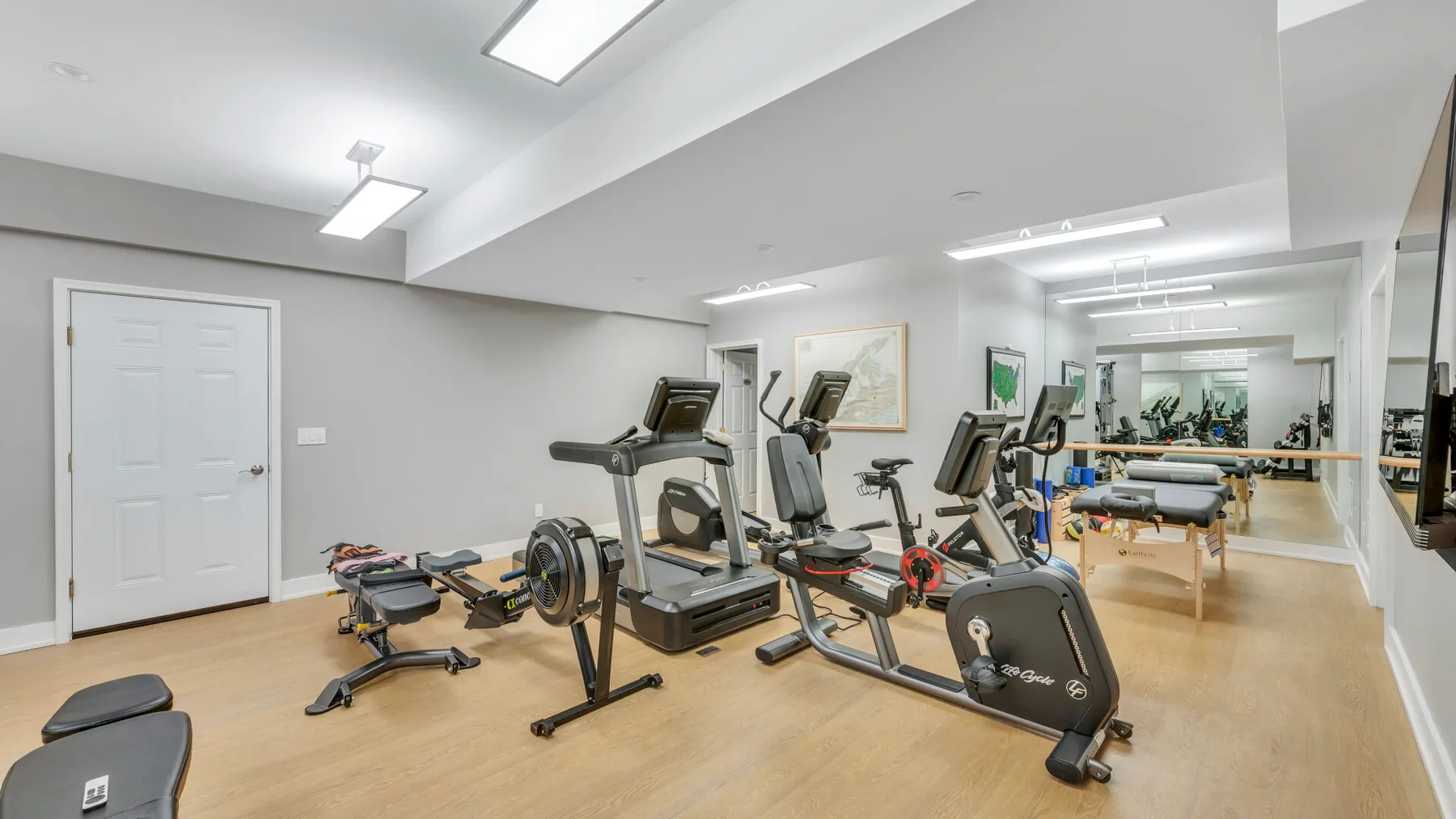 Un gimnasio interior luminoso con máquinas de ejercicio y una pared de espejos.
