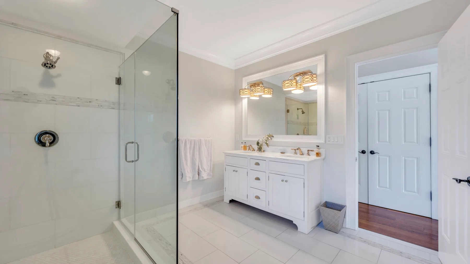 Un baño luminoso con ducha de vidrio, lavabo doble y armarios blancos.