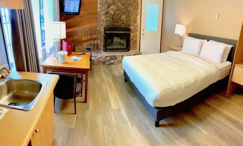 Cabin-style room with bed, fireplace, small kitchen and table.