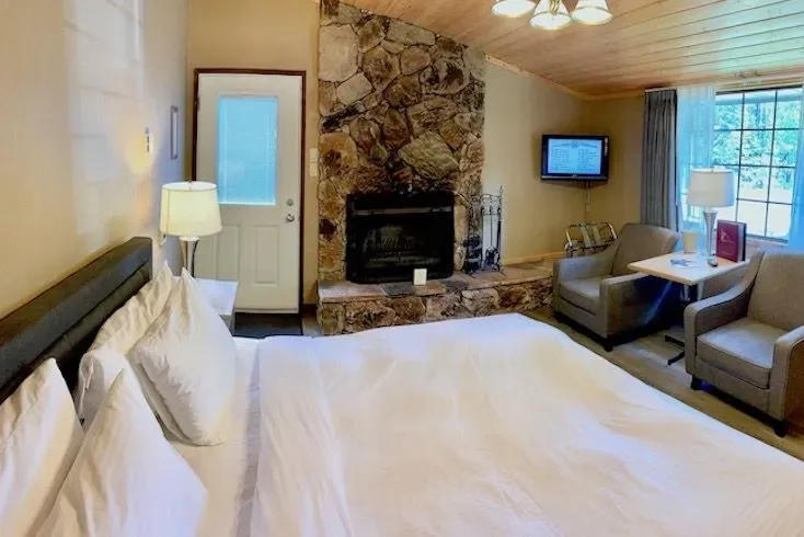 King room with a fireplace, bed, armchairs, TV and exterior door.