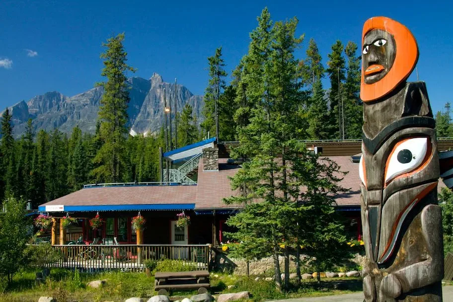 Lodge with a totem pole and mountains in the background.