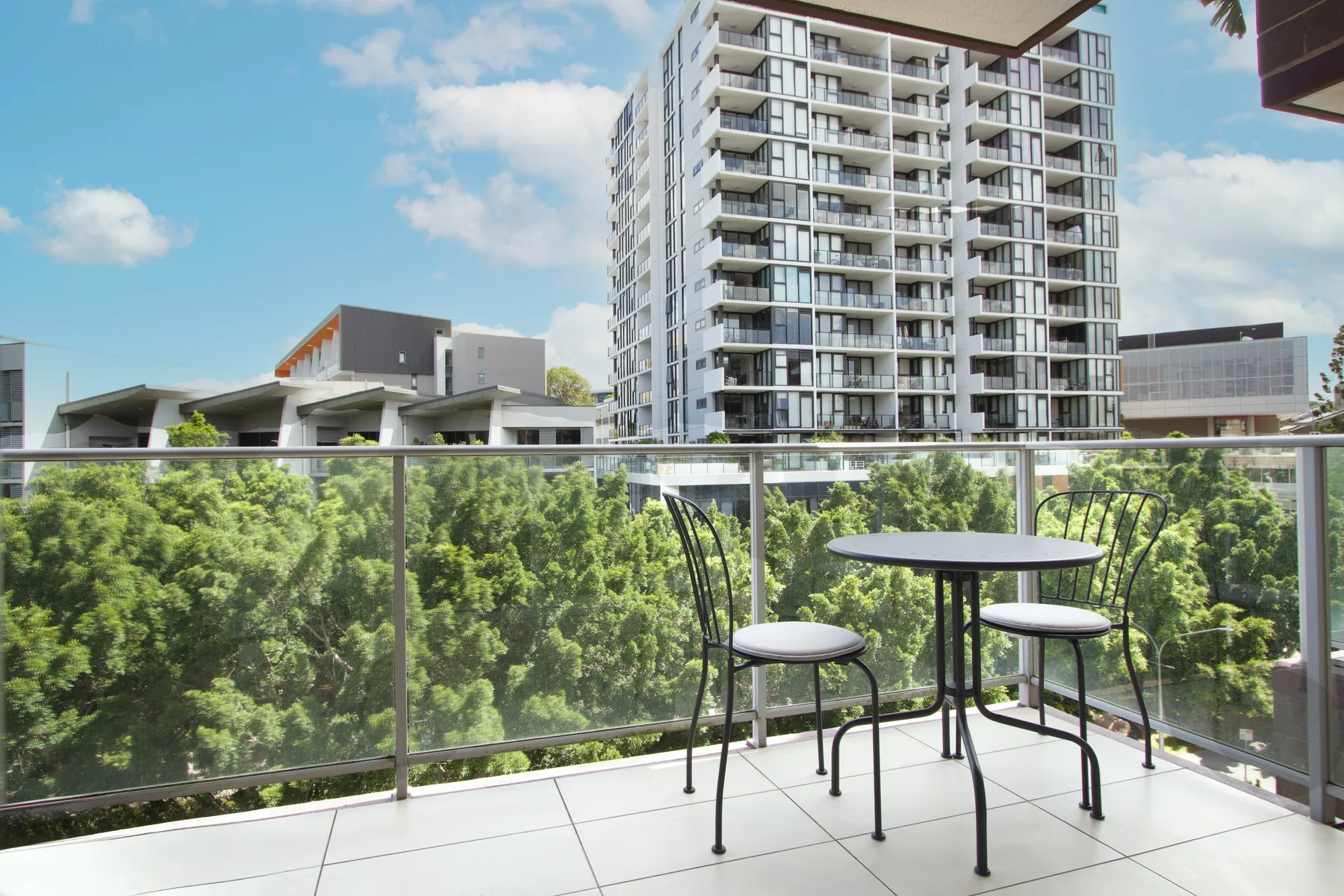 A balcony seating area overlooks leafy trees and a high-rise building.