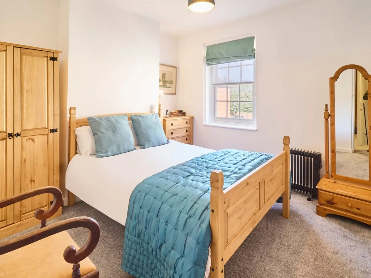 A bright bedroom with a wooden bed dressed in white and blue bedding.