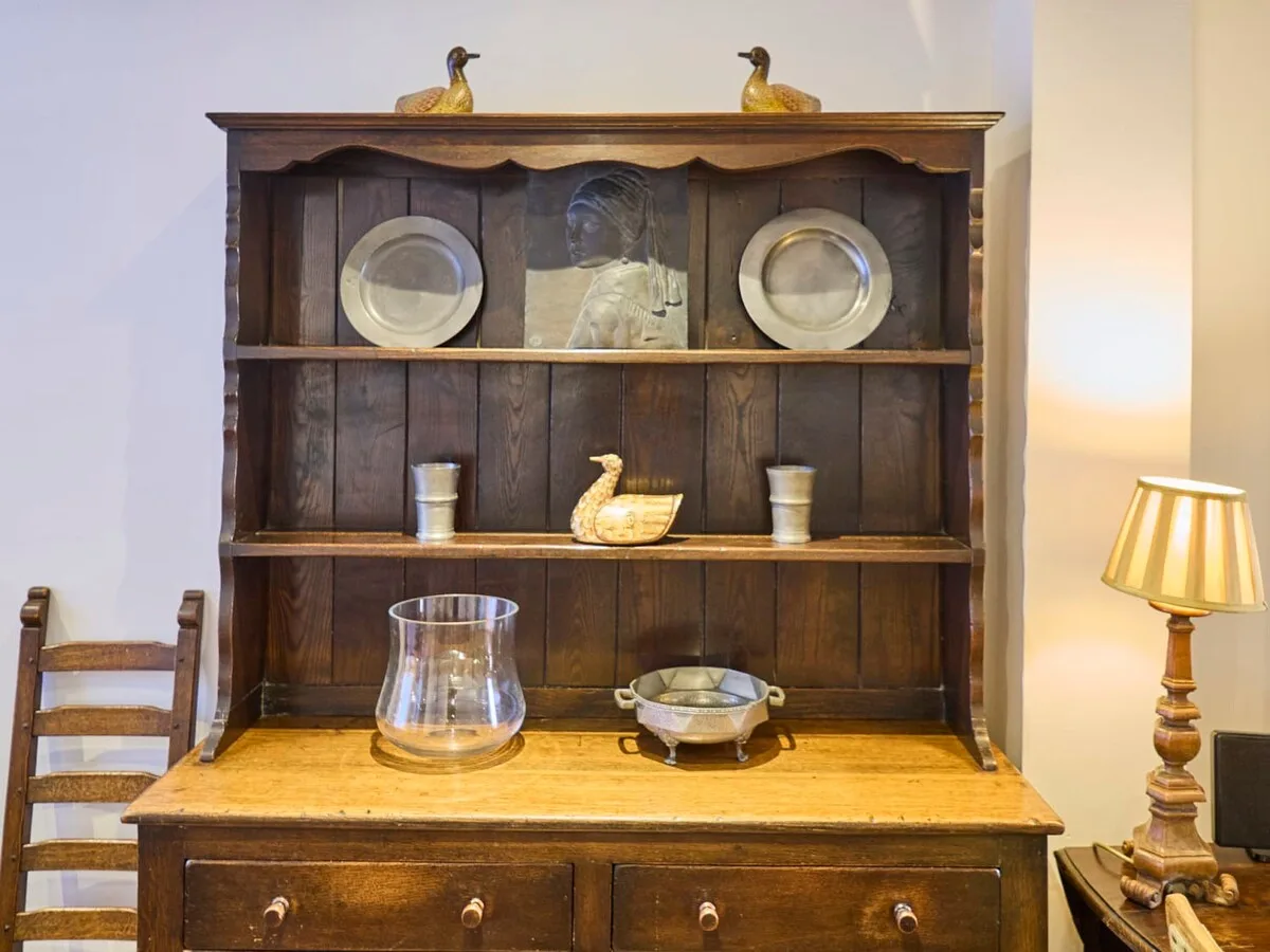 Un armario de madera está detrás de una mesa con cerámica y una lámpara.