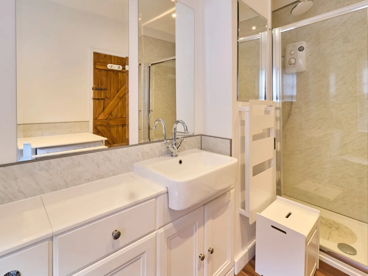 Un baño luminoso con lavabo, espejo y ducha de vidrio.