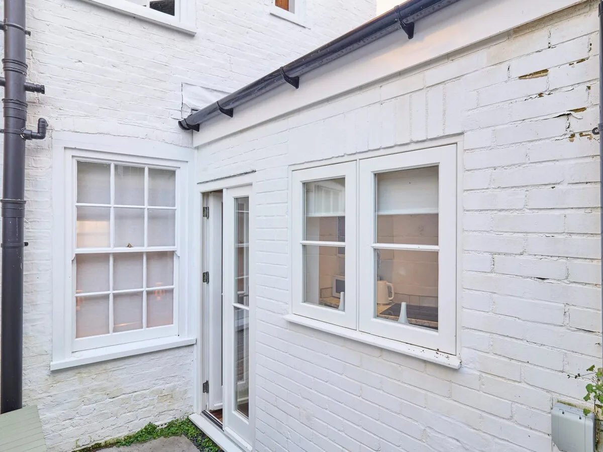 A small enclosed courtyard with white-painted brick walls, windows, and a narrow glass door.