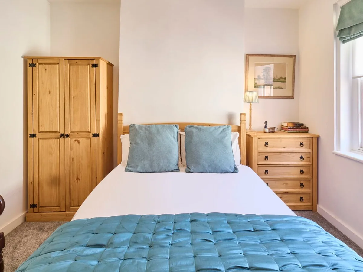 A bright bedroom with a neatly made bed and wooden furnishings.