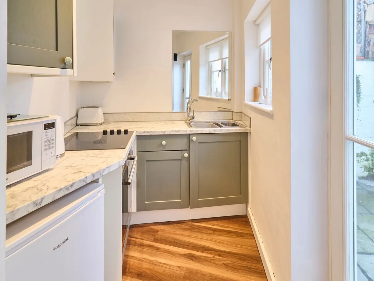 A compact kitchen with a countertop, sink, and windows.