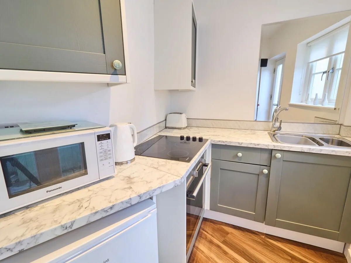 A bright kitchen with gray cabinetry, marble-patterned counters, and a window.
