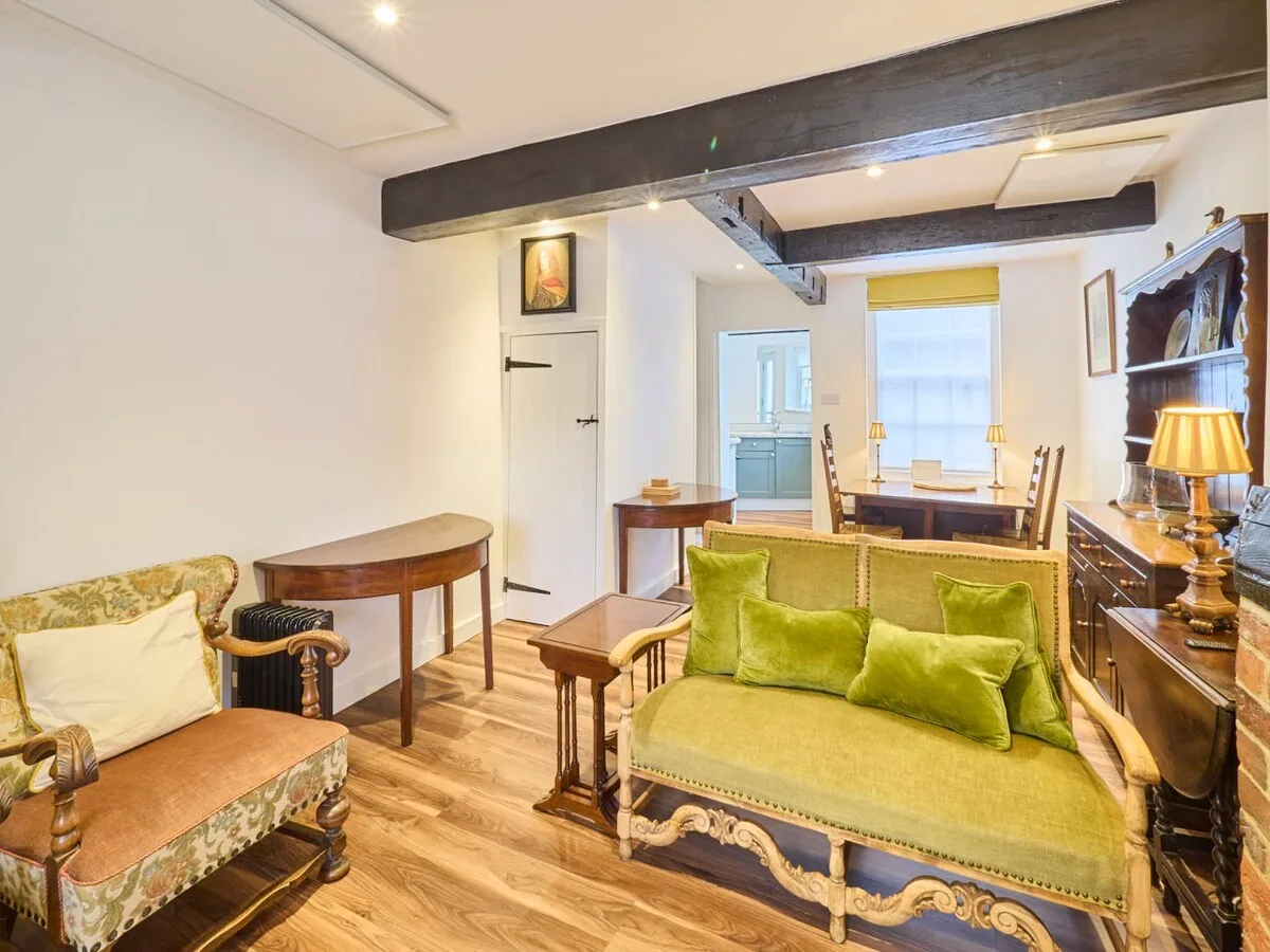 A living room with green seating, wooden furnishings, and exposed ceiling beams.