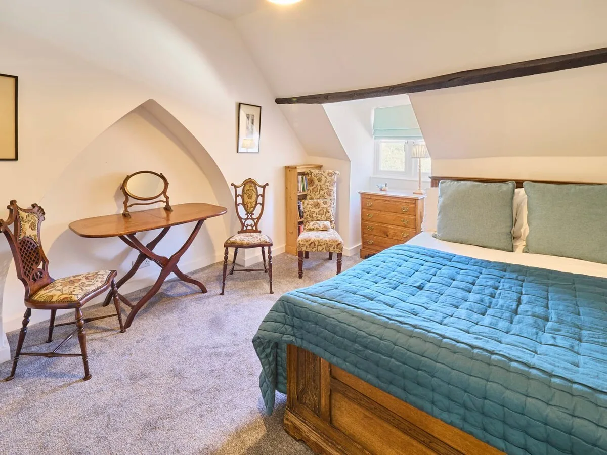 Un dormitorio con una cama, una mesa pequeña y sillas bajo un techo inclinado.