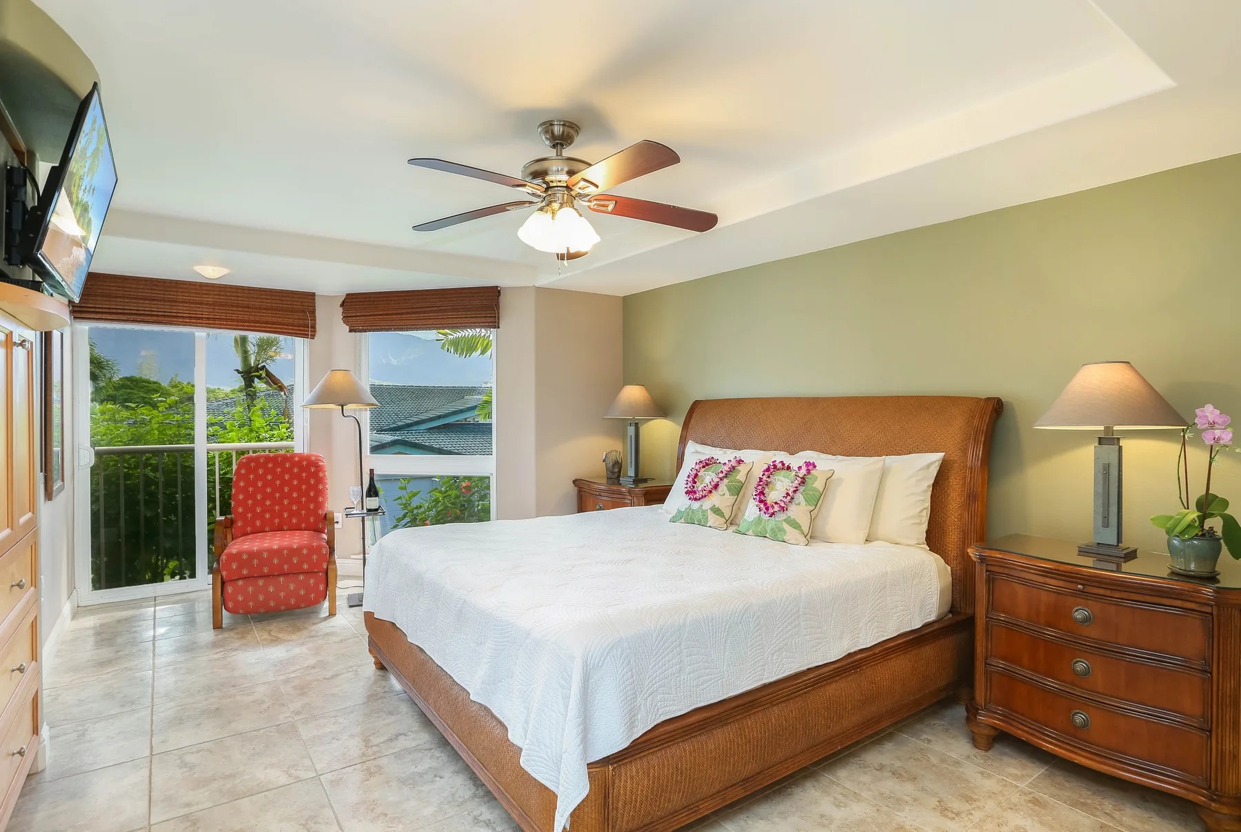A bedroom with a large bed, bedside tables, and windows overlooking greenery.