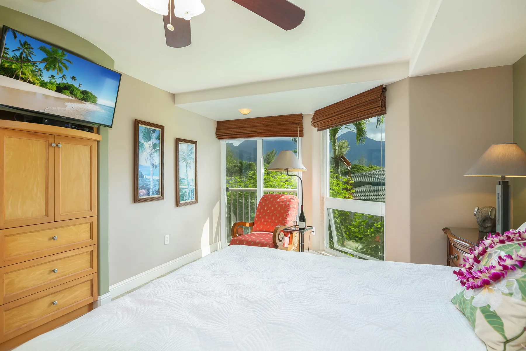 A bright bedroom with a white bed, a red chair, and large windows.