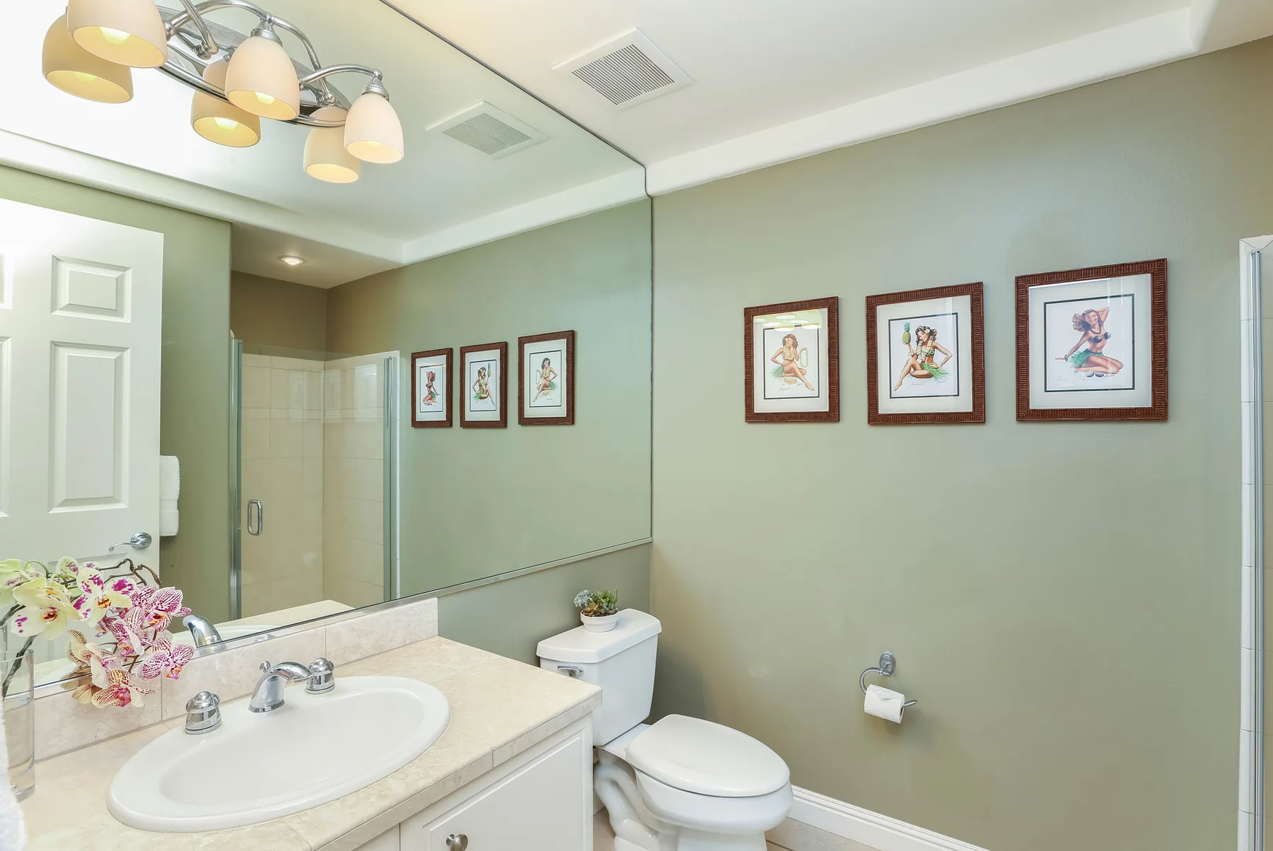 A bathroom vanity and toilet sit beneath a large mirror beside a glass shower.