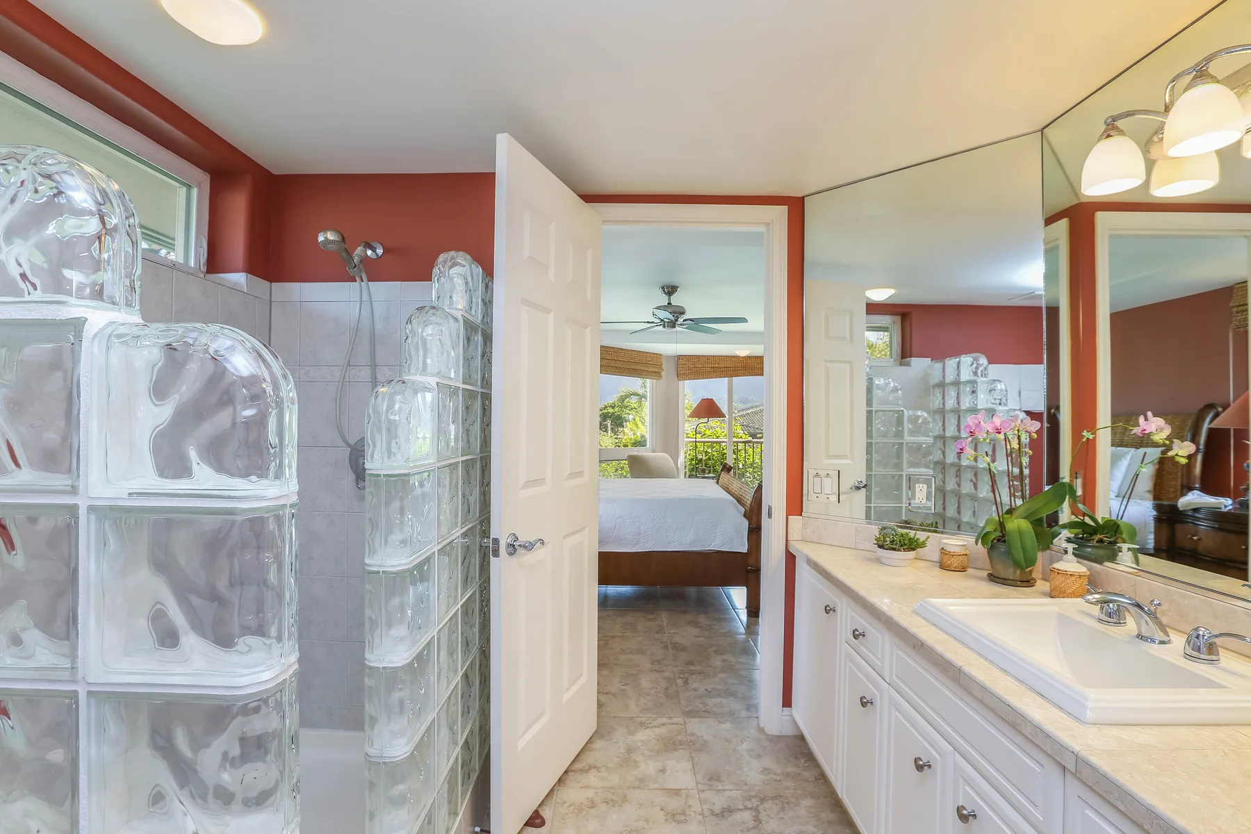 A bathroom vanity and glass-block shower are beside an open doorway to a bedroom.