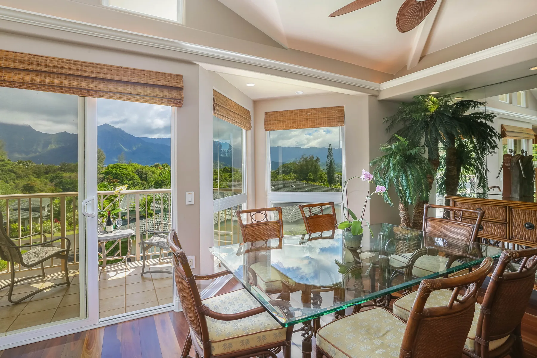 A bright dining area with a glass table and windows overlooking green mountains.