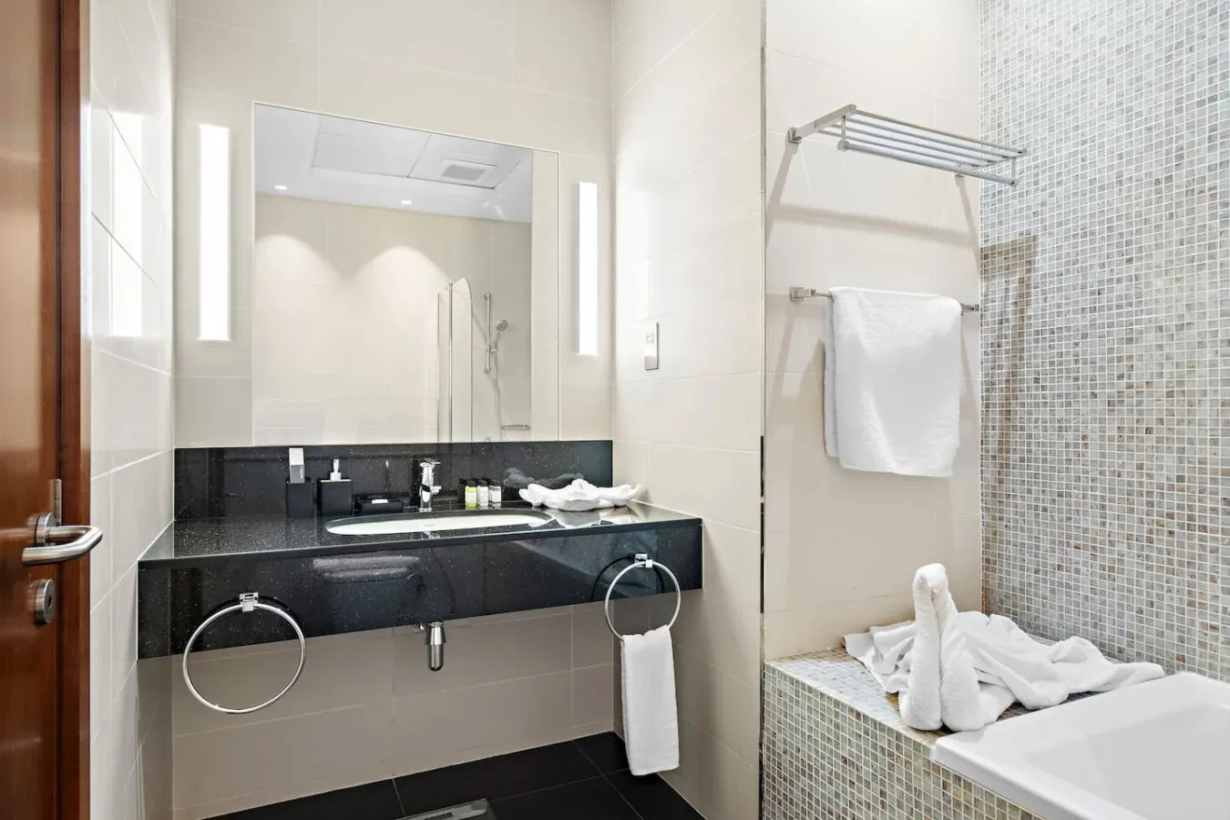 Un baño luminoso con un lavabo largo, espejo y zona de bañera con azulejos.