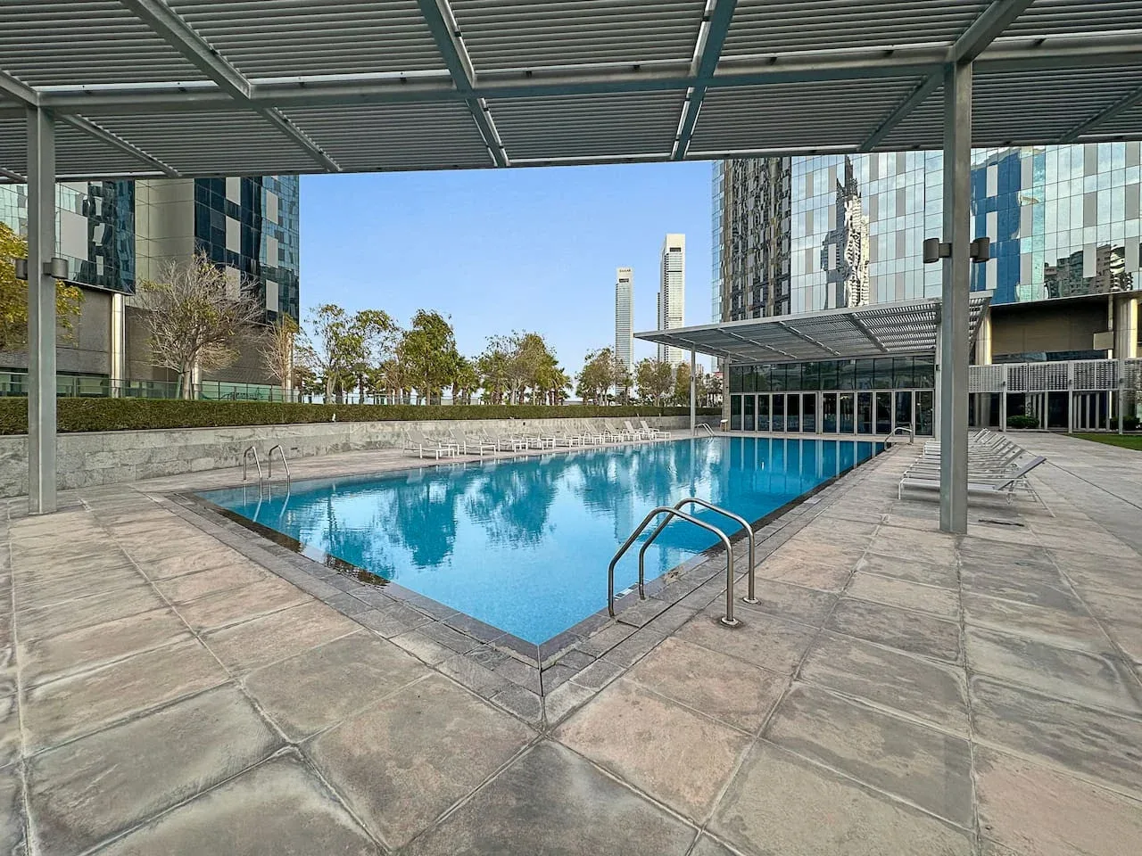 Una piscina al aire libre está bajo una cubierta junto a edificios modernos.