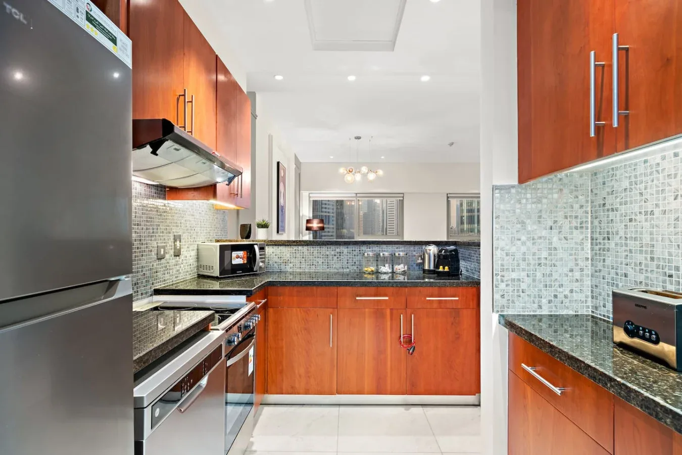 Una cocina moderna con gabinetes de madera rojiza, electrodomésticos de acero inoxidable y un salpicadero de azulejos.