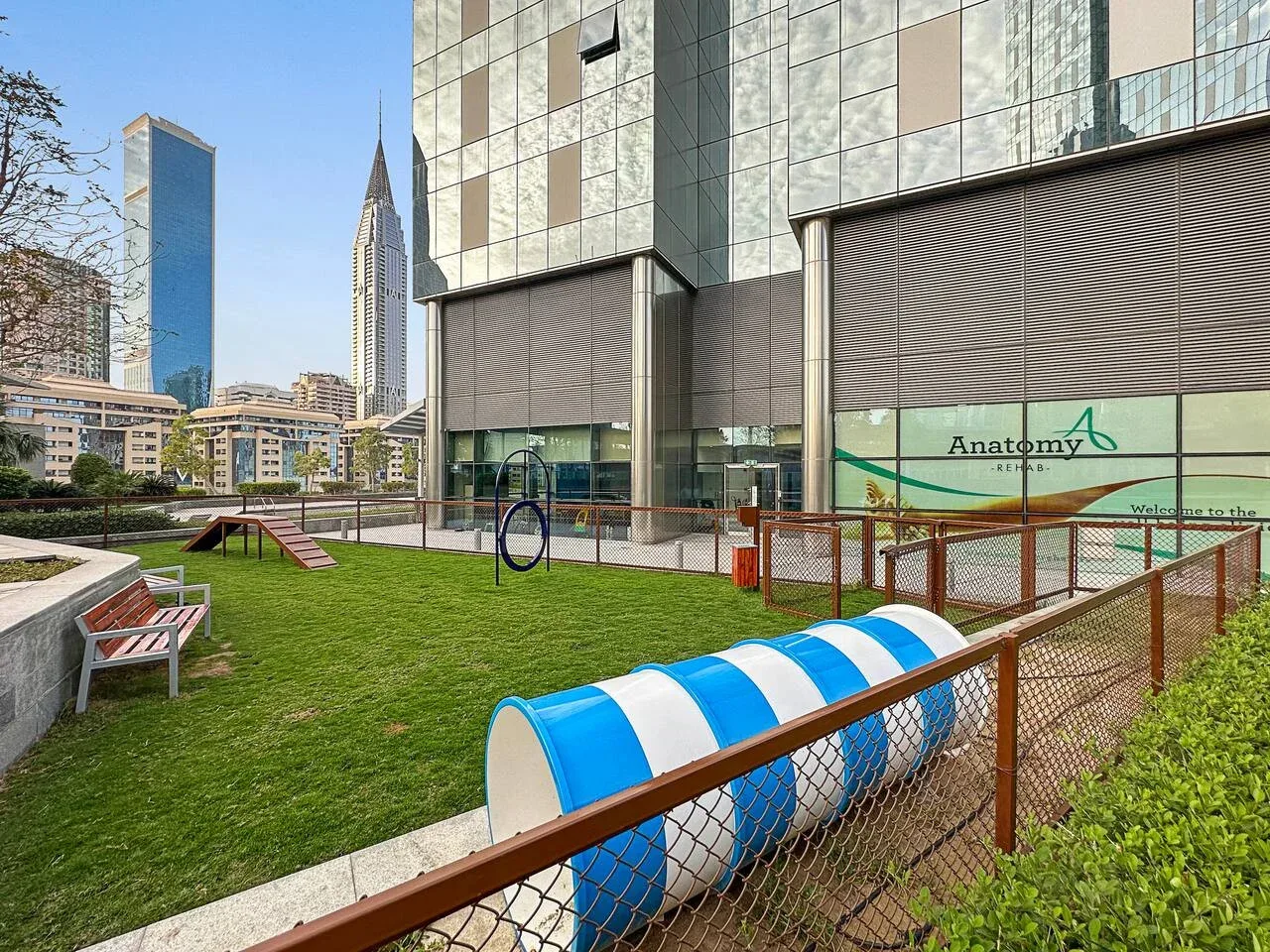 Una pequeña zona de juegos al aire libre con césped, juegos y edificios alrededor.