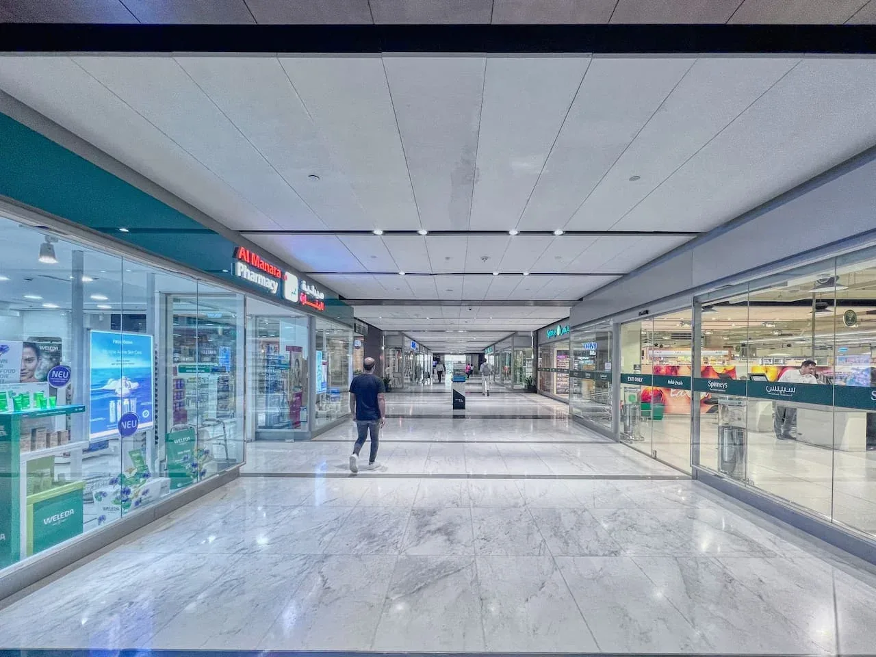 Un pasillo de centro comercial con escaparates de vidrio y suelo de piedra pulida.