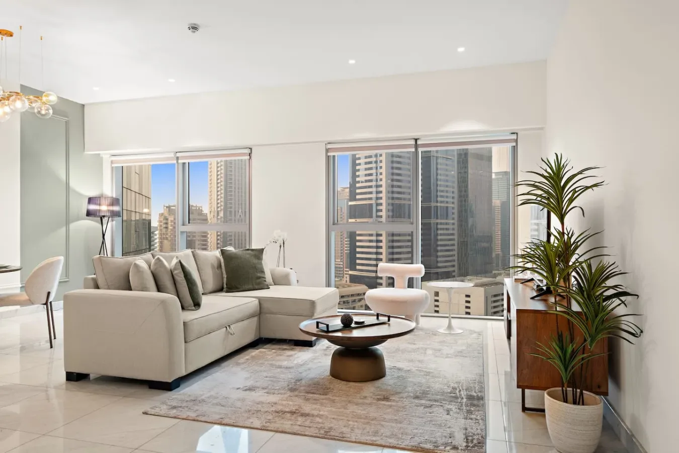 Una sala luminosa con sofá seccional, mesa de centro y grandes ventanas con vistas a la ciudad.