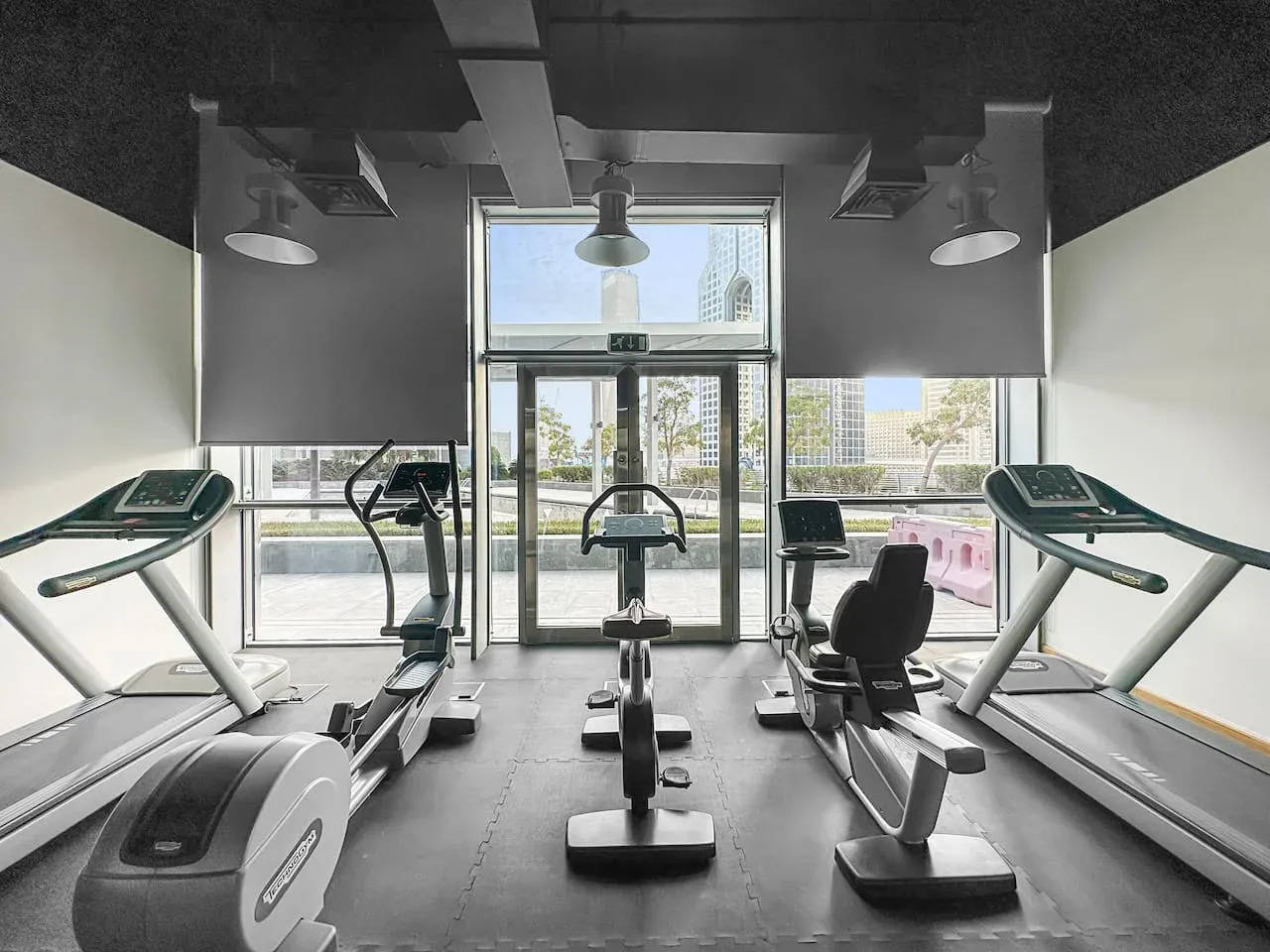 Un gimnasio con cintas de correr y otros equipos de ejercicio junto a grandes ventanales.