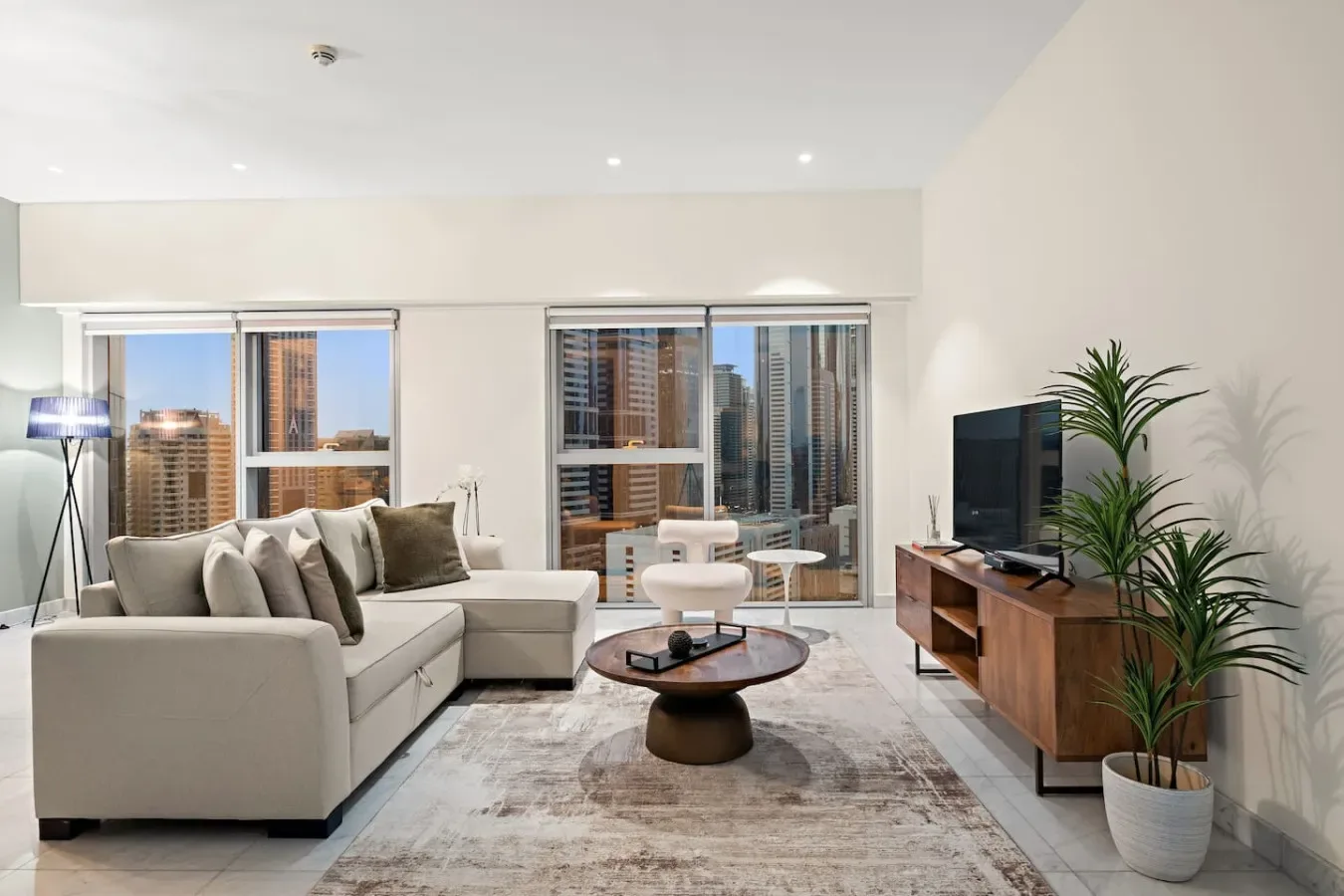 Una sala luminosa con asientos, una mesa de centro y grandes ventanas con vista a edificios de la ciudad.