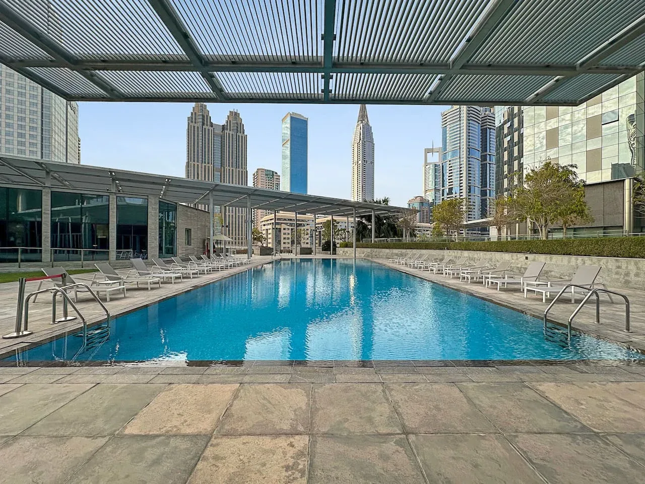 Una piscina al aire libre está rodeada de asientos y edificios de la ciudad.