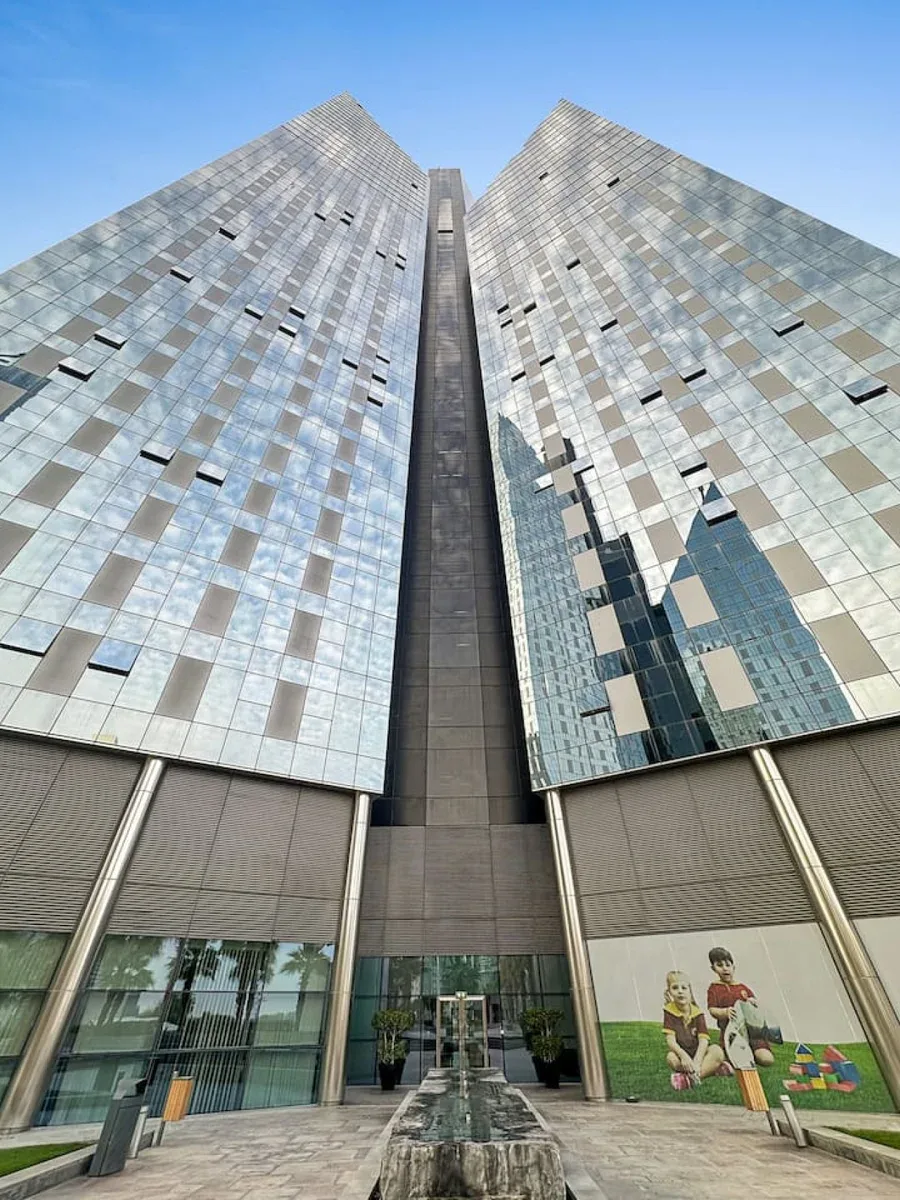Un edificio moderno de gran altura con ventanas reflectantes se alza sobre una entrada pavimentada.