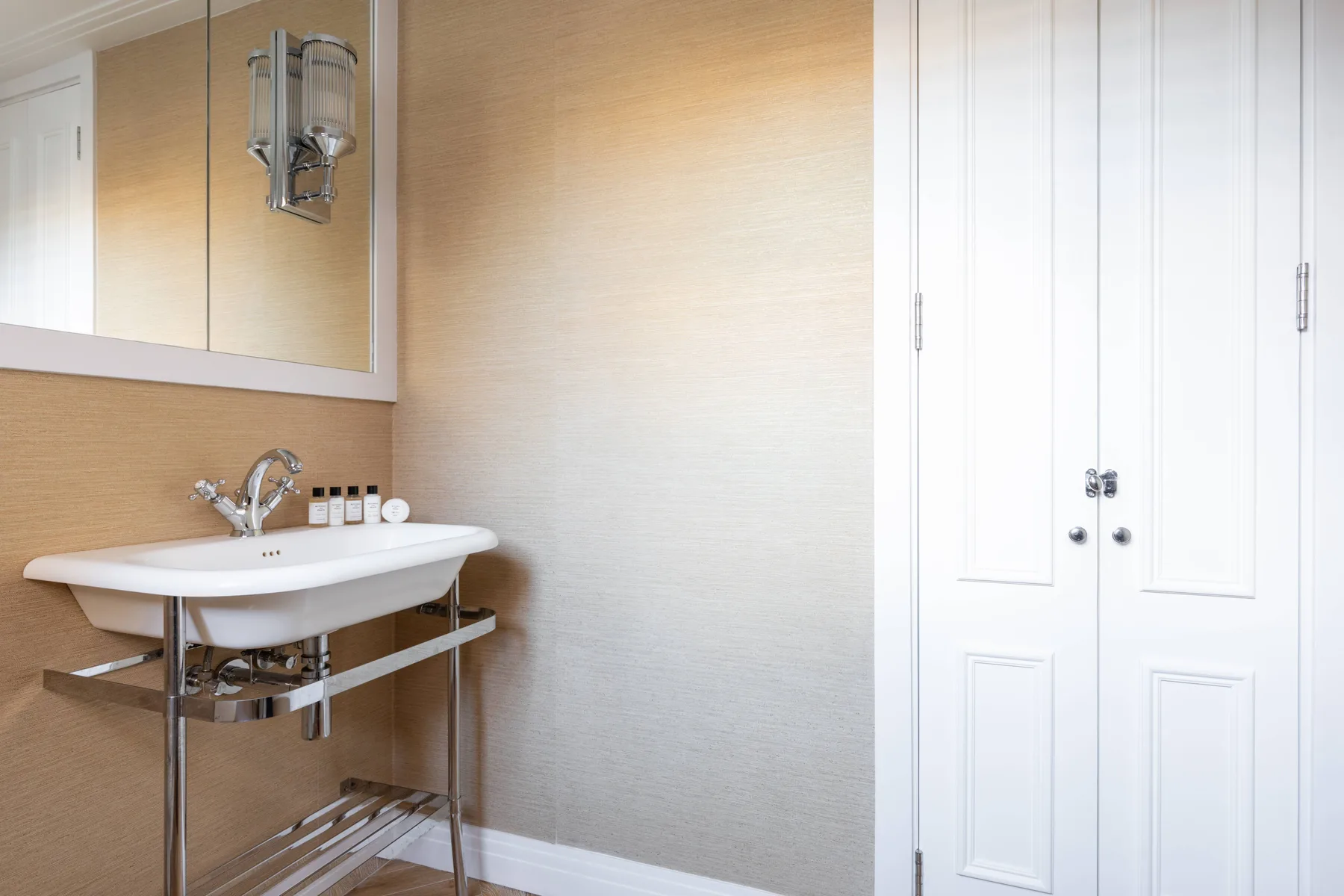 A bathroom with a wall-mounted sink, mirror, and white paneled doors.