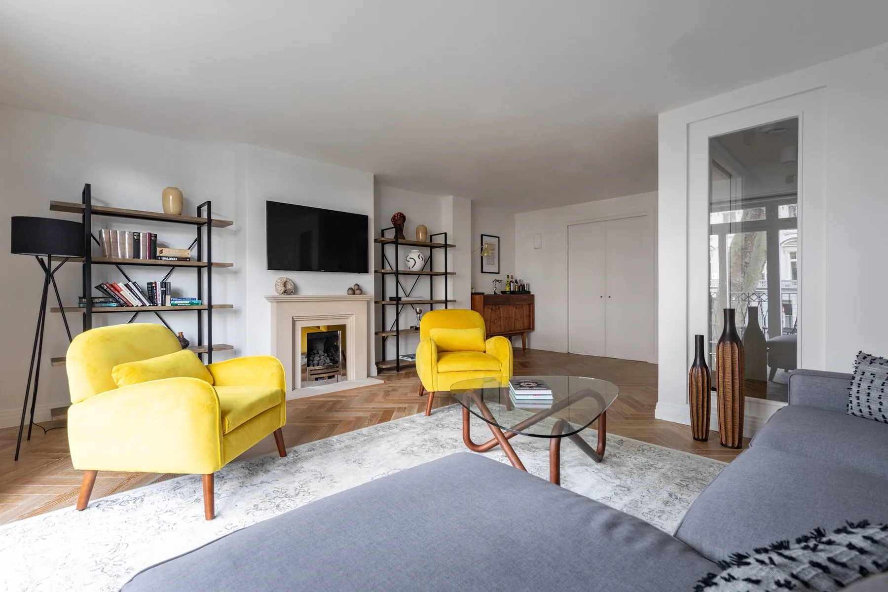 A bright living room with yellow seating, a fireplace, and a glass coffee table.