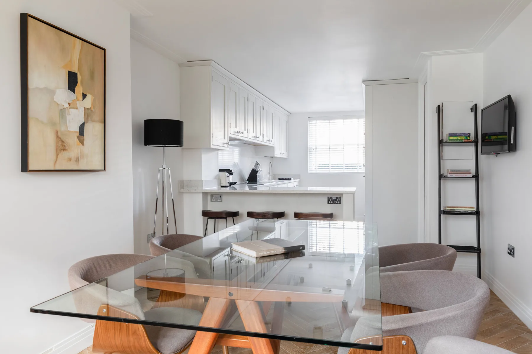 A dining area with a glass table and seating sits beside a bright white kitchen.