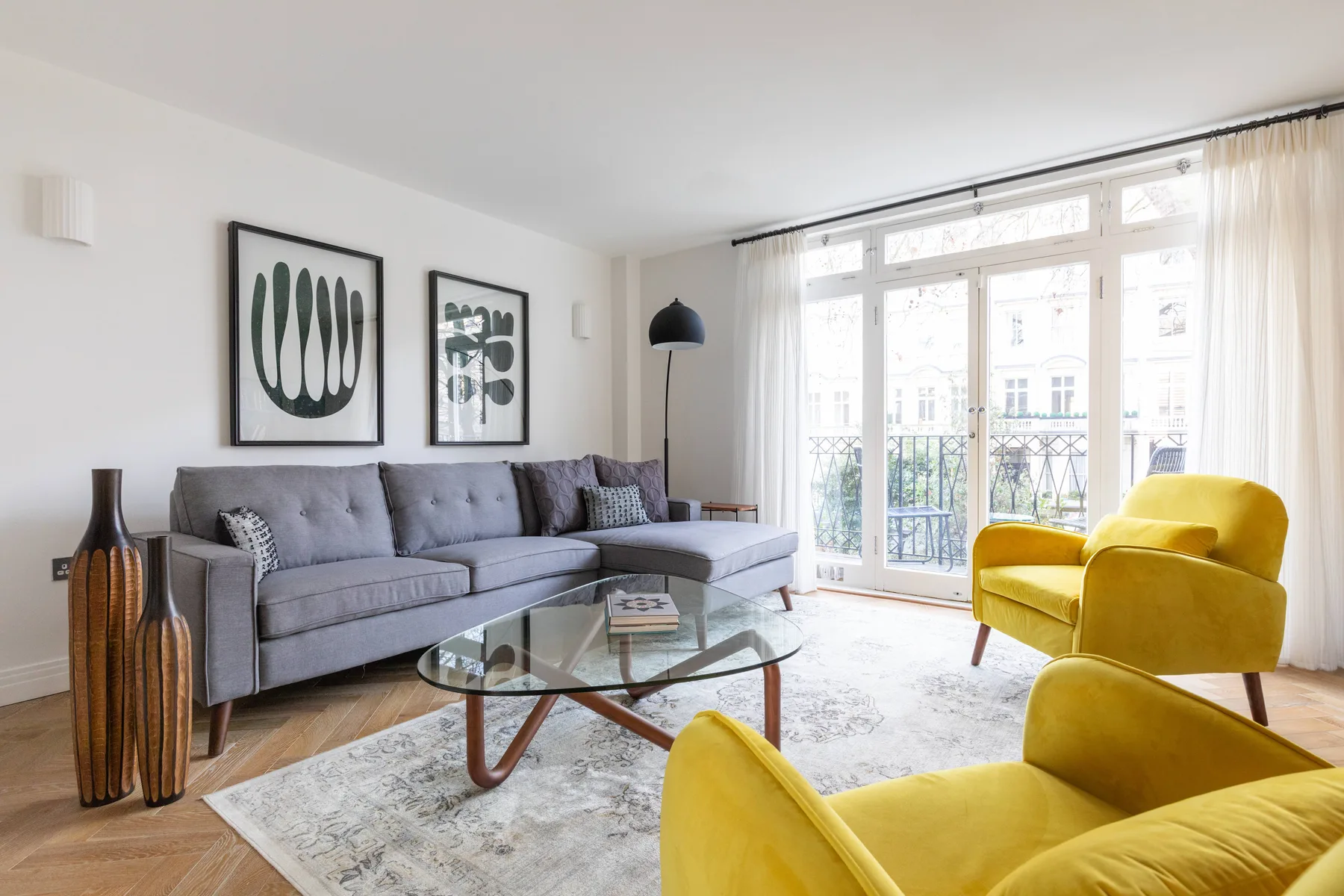 A bright living room with gray seating and yellow armchairs beside large windows.