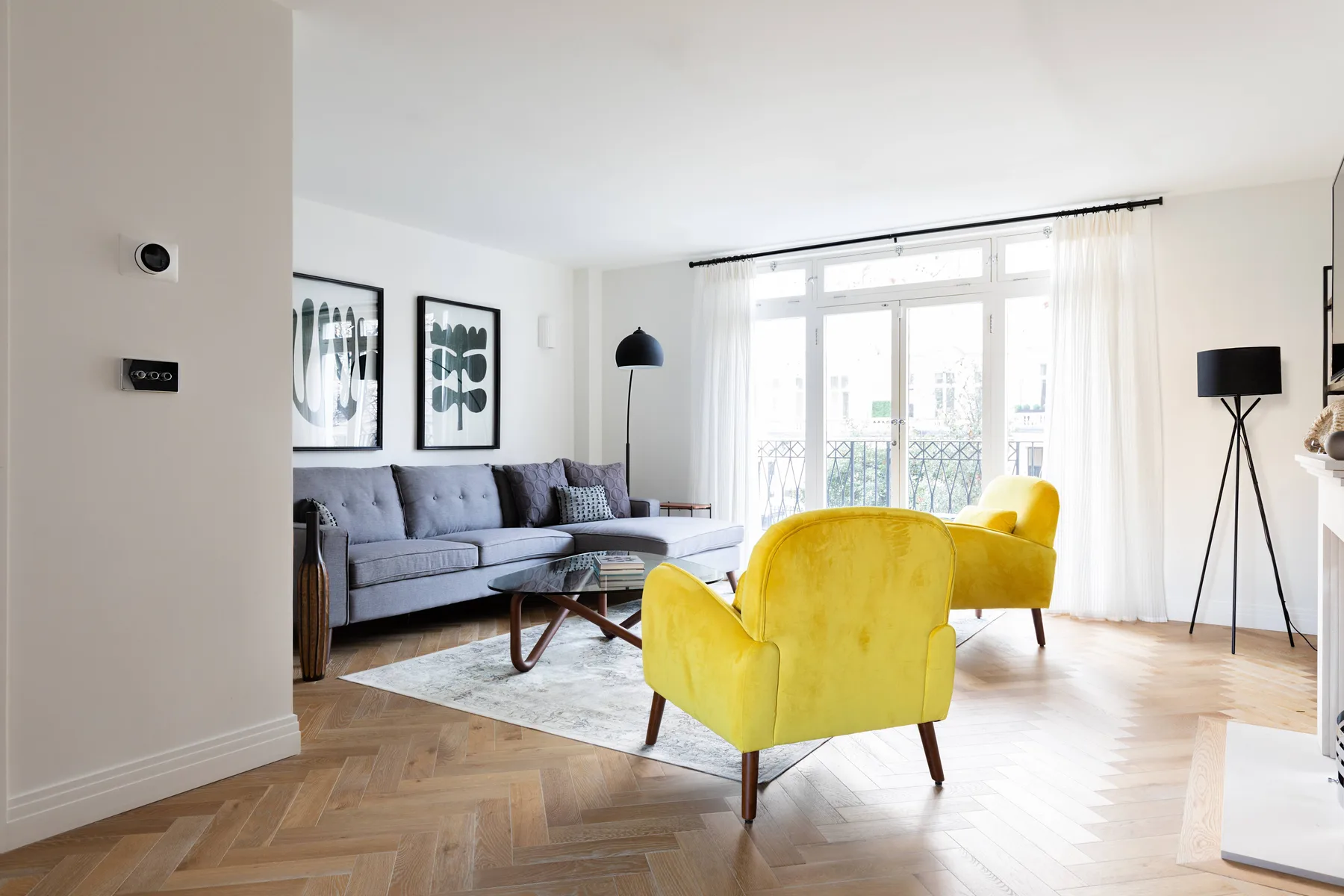 A bright living room with a gray sofa and yellow seating beside large windows.