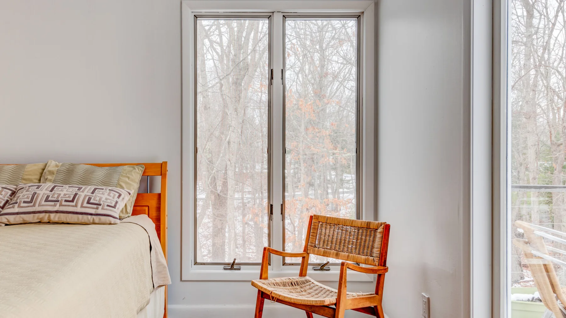 A bedroom with a bed and a wooden chair beside large windows.